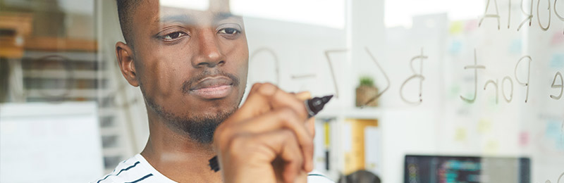 Male entrepreneur writing on a whiteboard listing out the technology features and uses for his business.