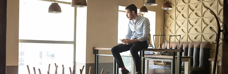 Male entrepreneur siting on top of table in closed restaurant. Muling over why the plan they created failed.