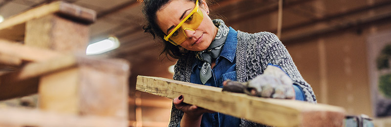 Female entrepreneur in a carpentry shop working on cutting a piece of wood. She has a firm understanding of her industry to grow her business.