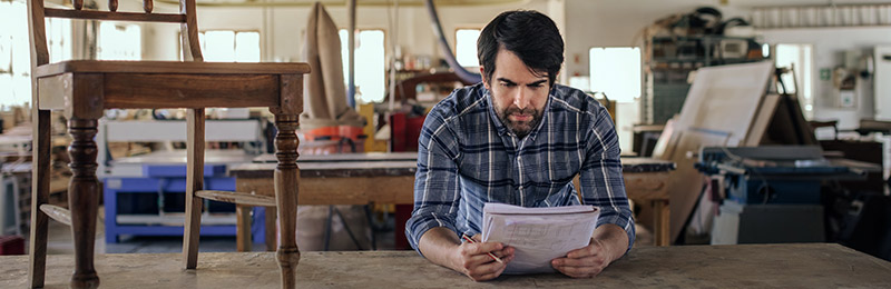 Male entrepreneur in workshop standing at a table reviewing his lean business plan.