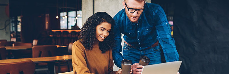 Male and female entrepreneurs sitting in a restaurant developing a digital marketing strategy on their computer.