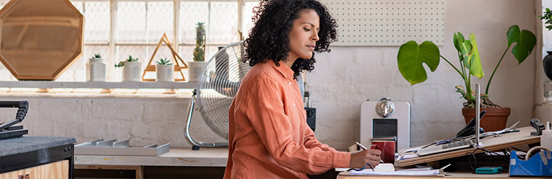 Female entrepreneur sitting within a home studio drafting up individual plans for her business.